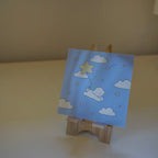 Small wooden easel with a blue art  featuring stars and clouds and a dog.