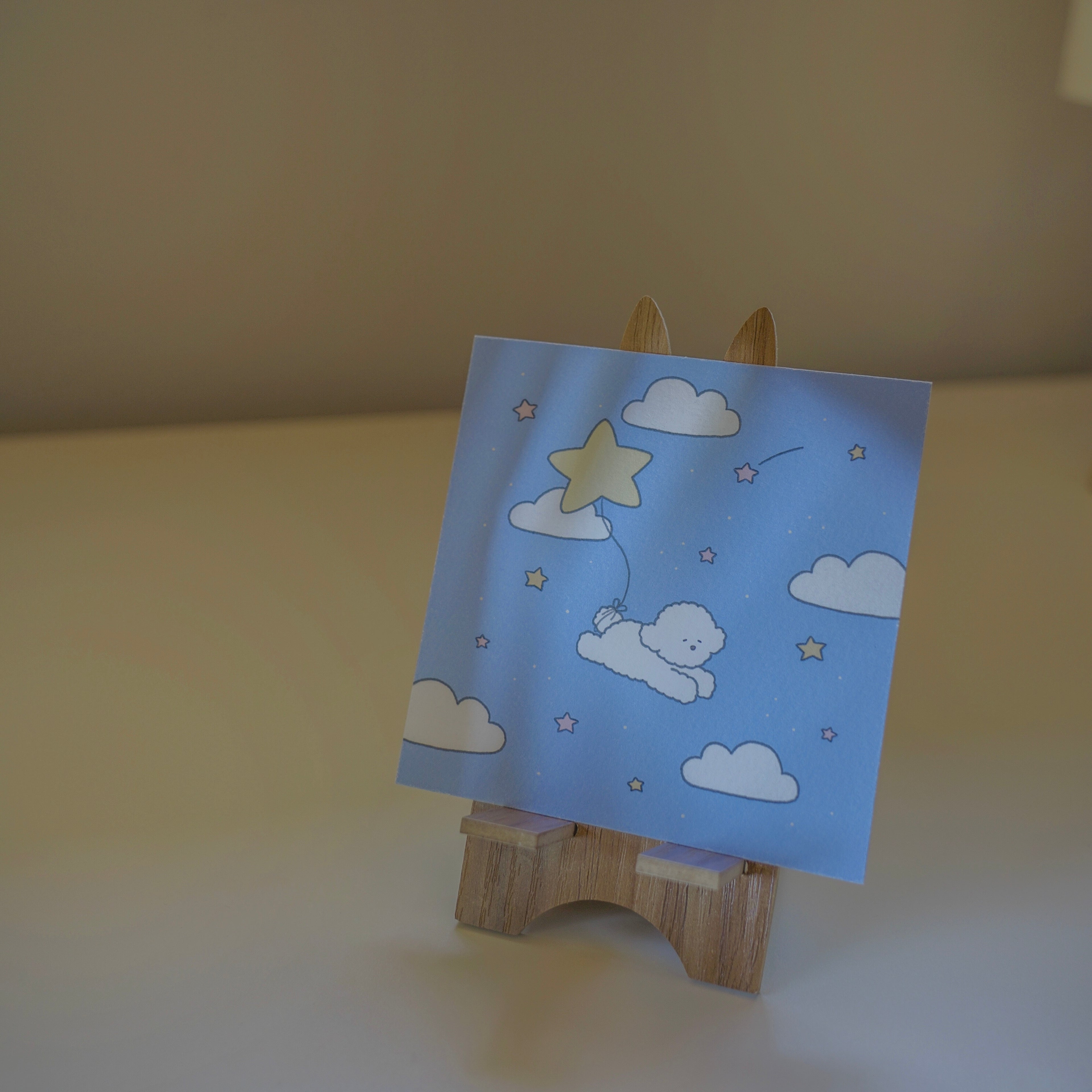 Small wooden easel with a blue art  featuring stars and clouds and a dog.