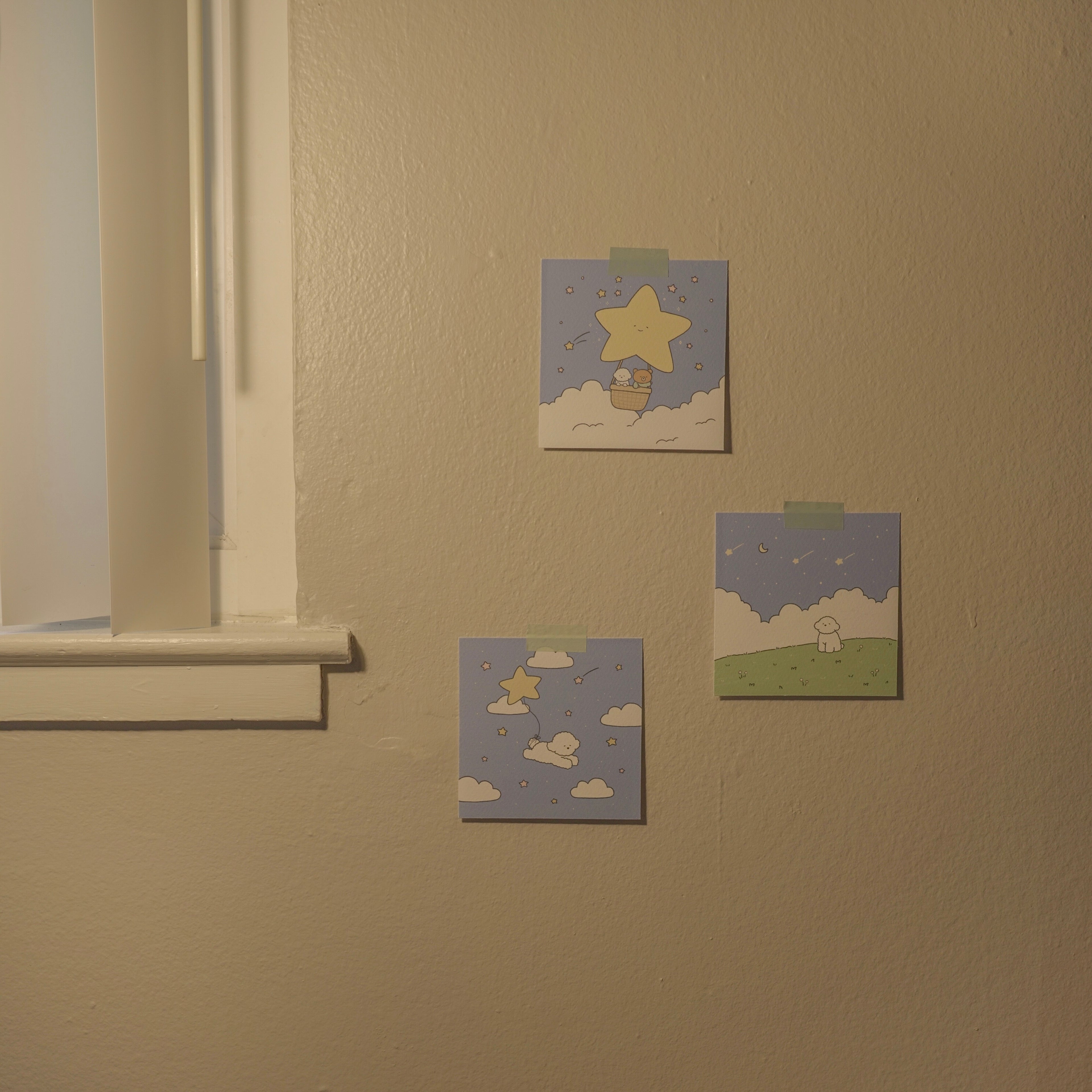 Three small artworks on a beige wall near a window.