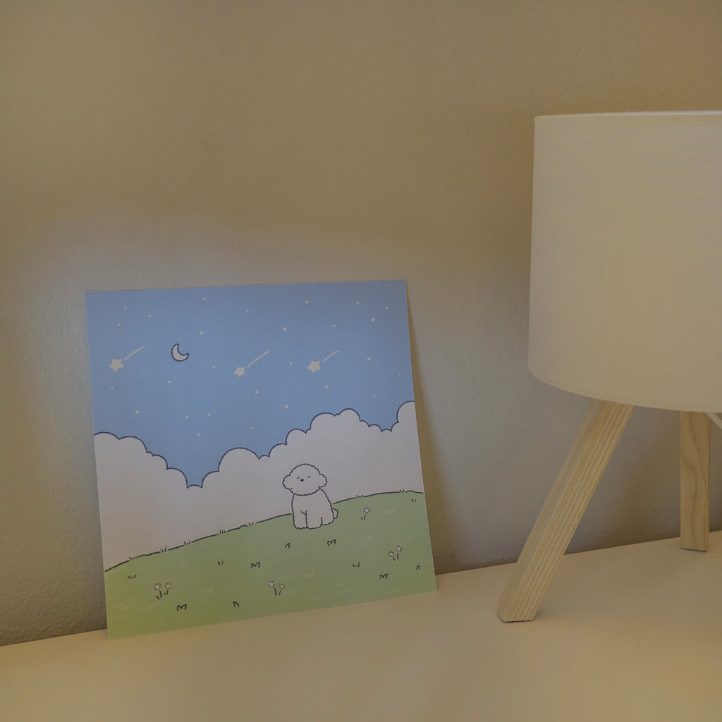 Illustrated print with a dog on a grassy field under a starry sky, next to a lamp.