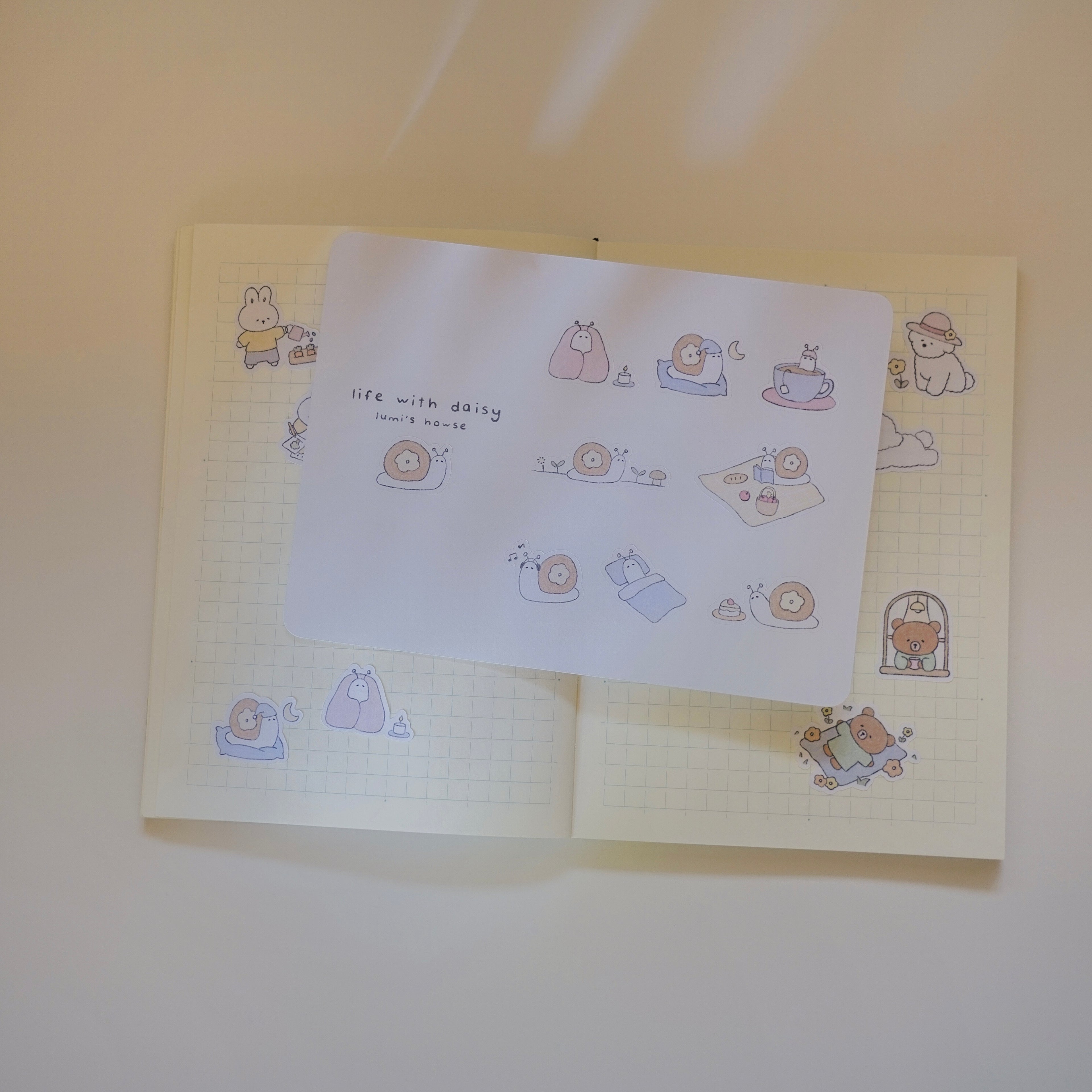 Open notebook with grid spaper and cute illustrations on a sticker sheet with a plain background.